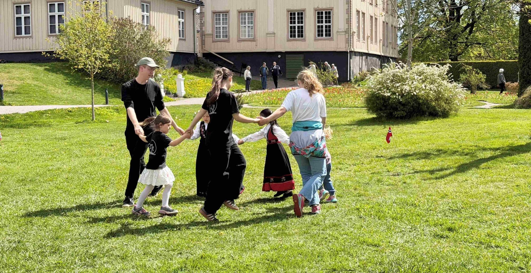 Askeladden leikarring - Småhalling, dans for små føtter. Voksne og barn danser på gressplenen utenfor herskapshuset i Brekkeparken