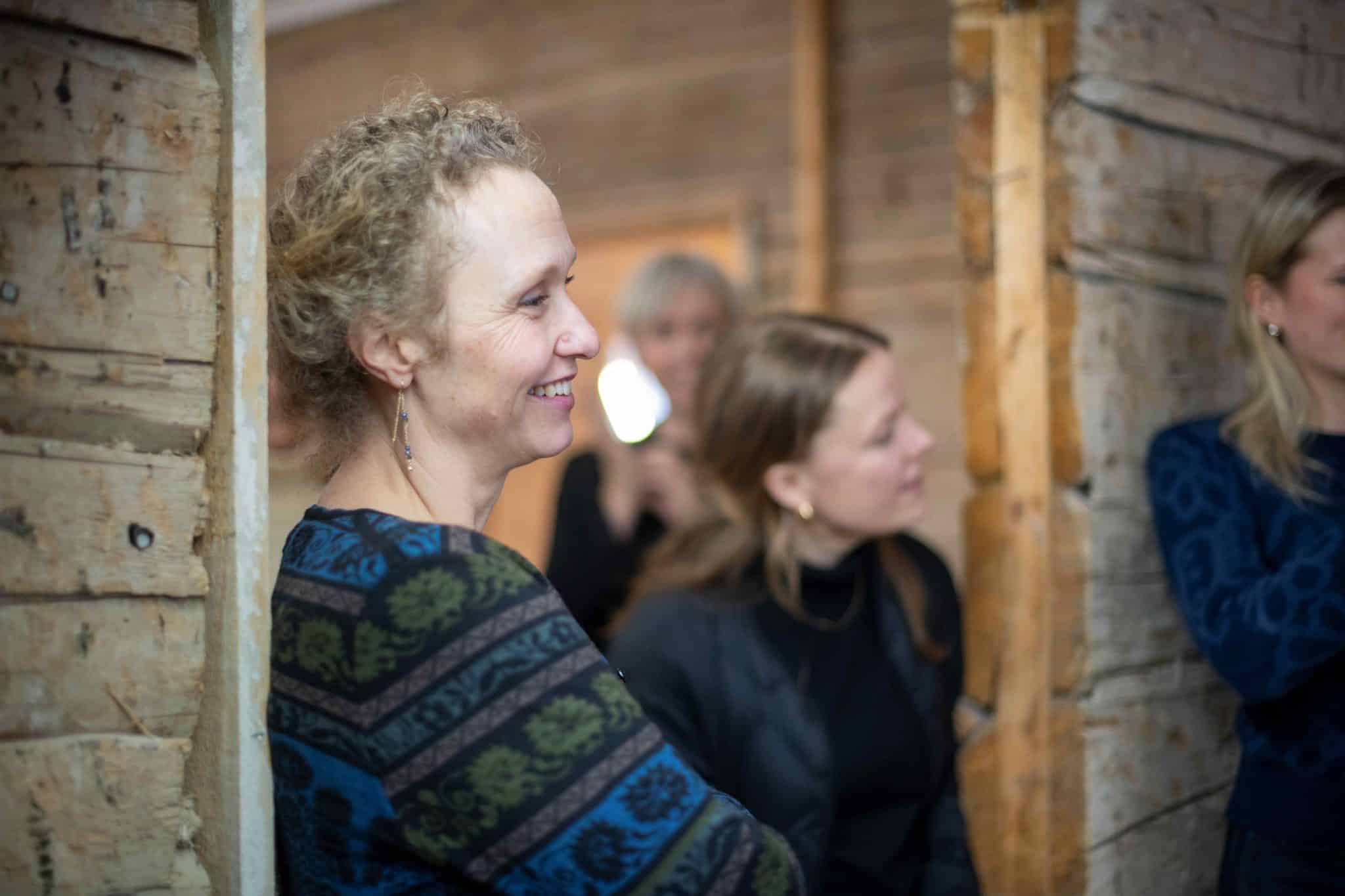 Christine Hermansen står lent mot en vegg. Smiler