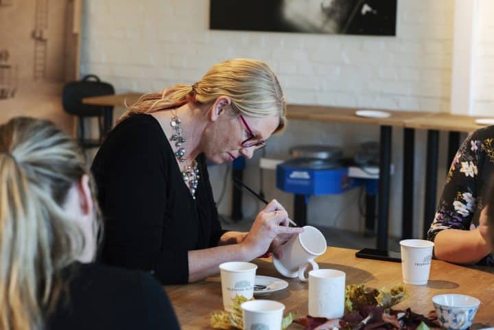 Workshop i porselensmaling. En kvinne sitter og maler på en hvit porselenskopp.