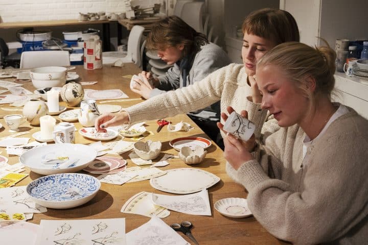 Mønster-workshop på Porselensmuseet. En gruppe ungdommer sitter rundt et bord med mange ulike mønster på papir som de skal dekorere porselenskopper med.