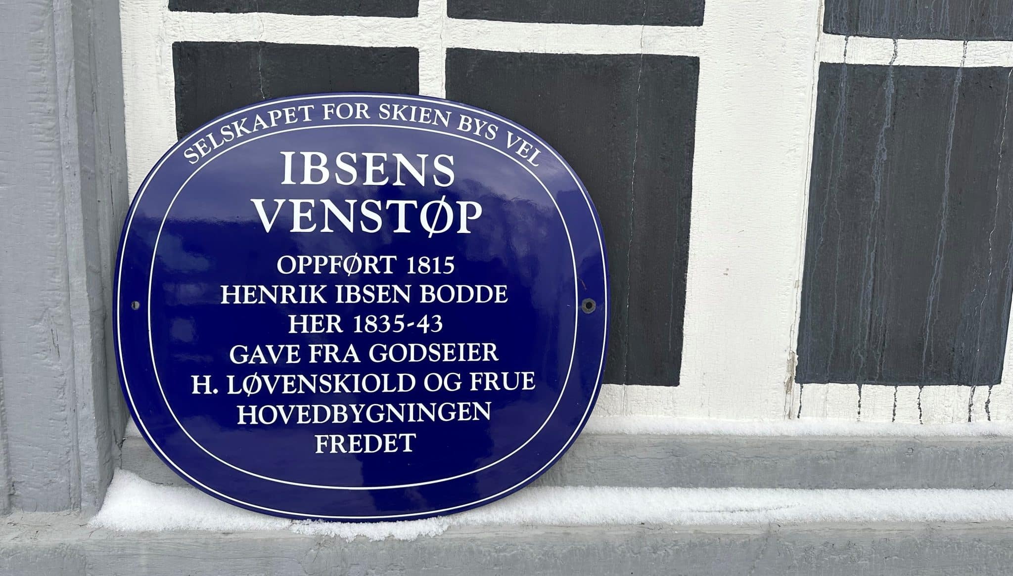 Det blå skiltet til Ibsens Venstøp, der det står at huset er oppført i 1815, Henrik Ibsen bodde her 1835-43, og at det er en gave fra godseier H. Løvenskiold og frue. Bygningen er fredet.