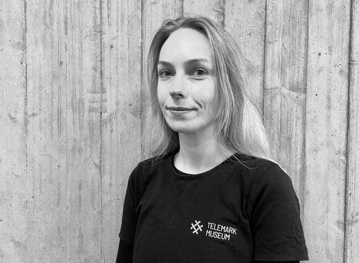 Sort-hvitt portrett av Ellen Marie Pettersen. Langt, lyst hår, blikket festet i kamera, svart telemark museums-genser