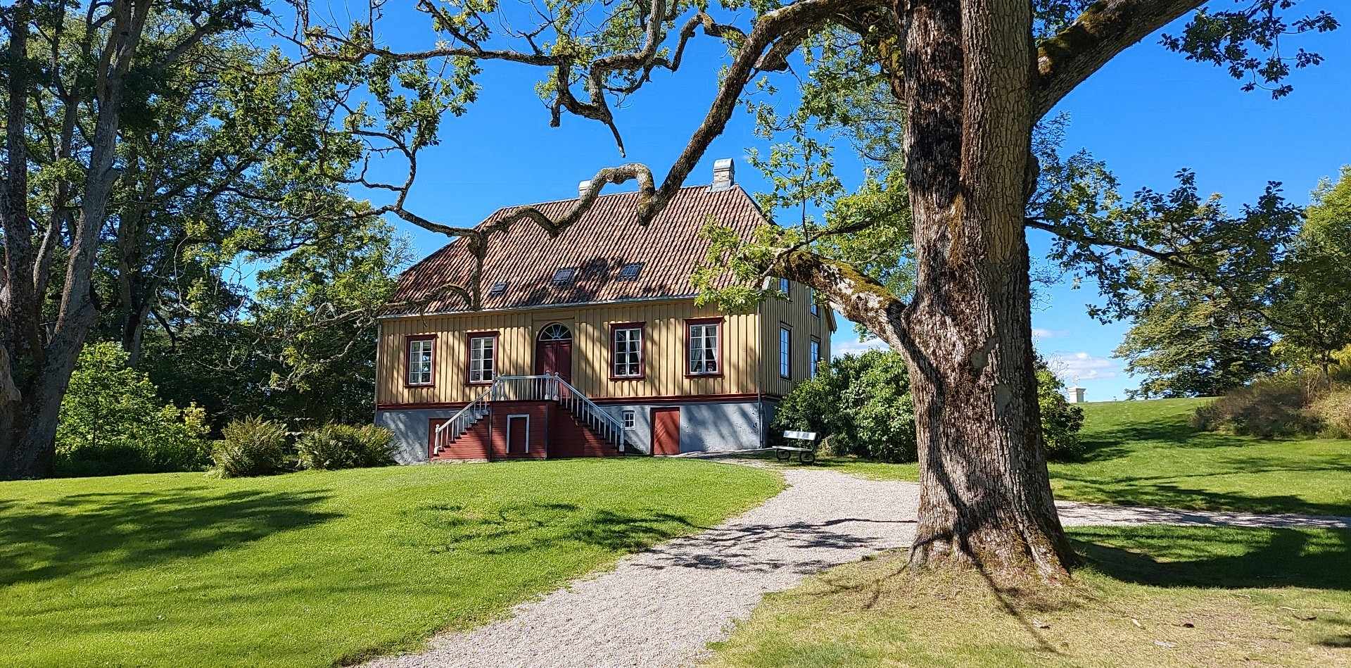 Hovedhuset på Lystgården på Berg-Kragerø Museum. Vi ser en grusvei som går opp mot huset. Foran huset, ved grusveien ser vi en av de mange, gamle eikene på eiendommen.