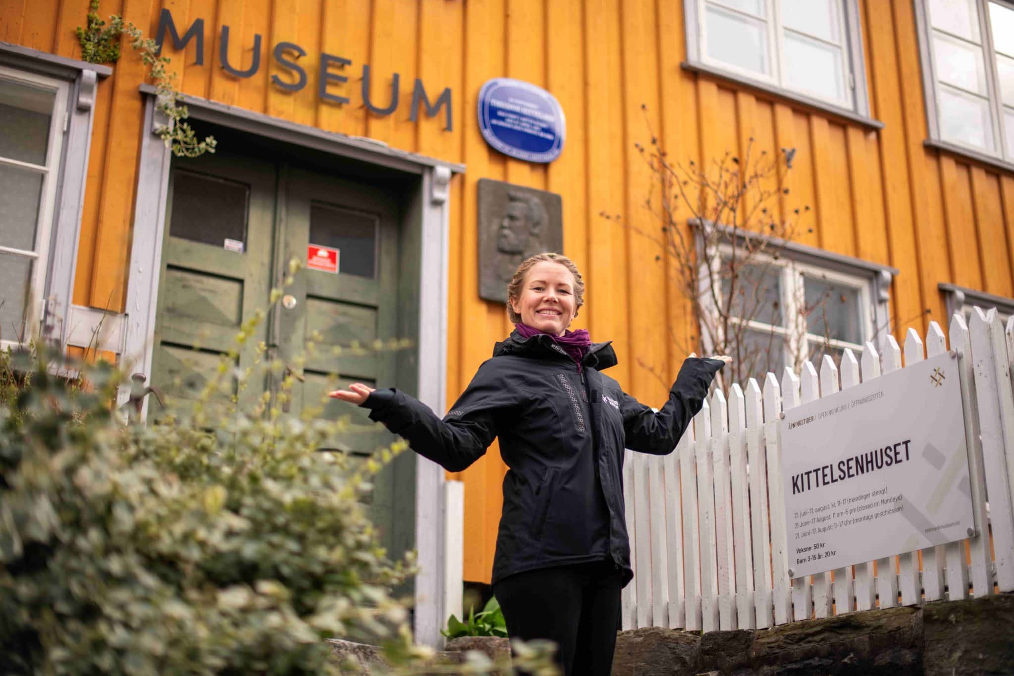 Karen Kjeøen Erikstad ønsker velkommen til Kittelsenhuset Foto MulleMedia. Karen står foran inngangen til museet, det gule,lille huset i Kragerø sentrum