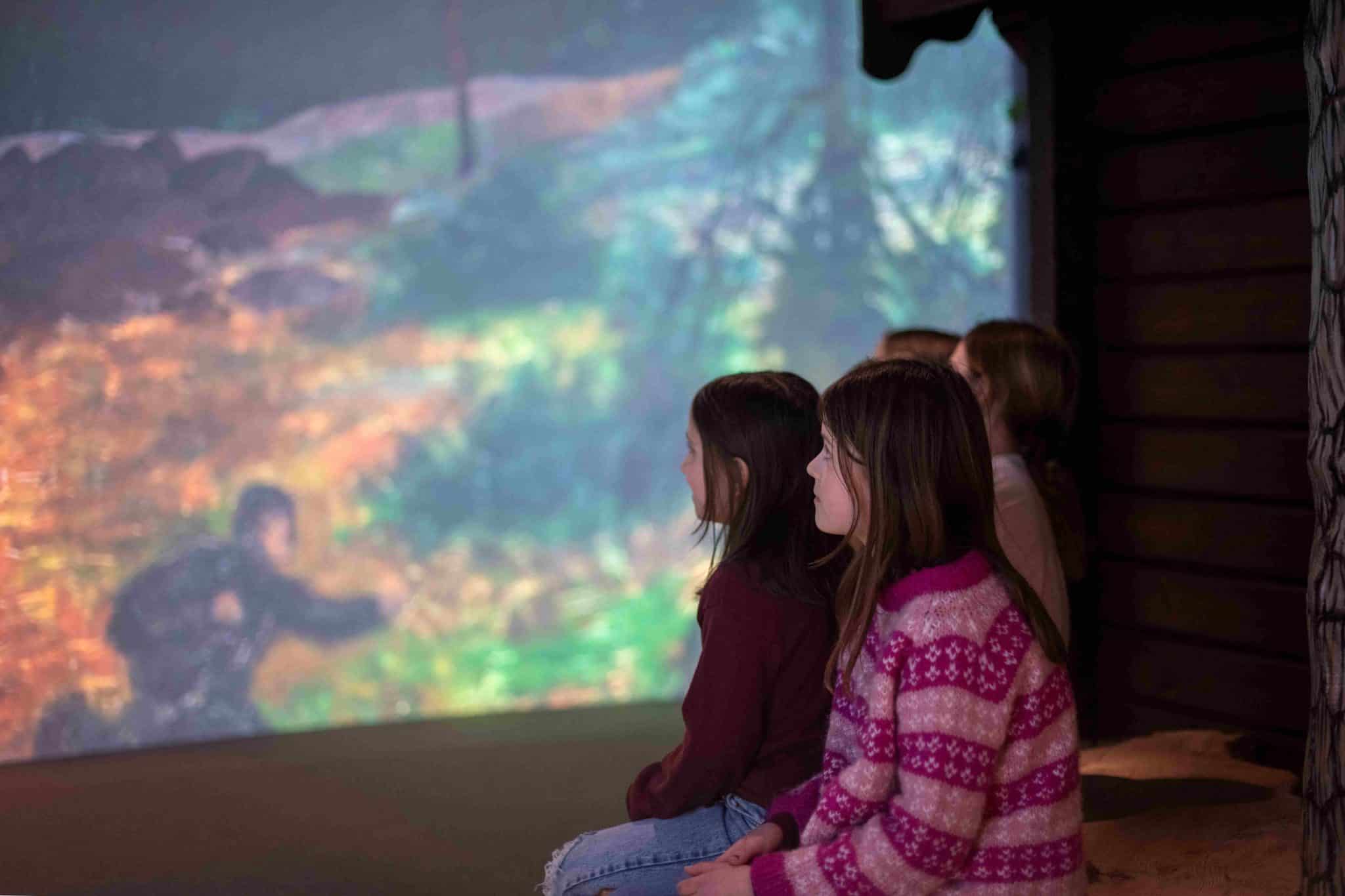 Eventyrlige Kittelsen. Noen barn sitter på gulvet og ser på en film, projisert på veggen