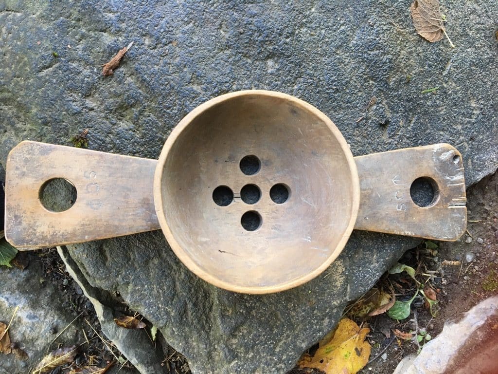 Gammel melkesil i tre med to håndtak på. Fem runde hull i bunnen av silen.