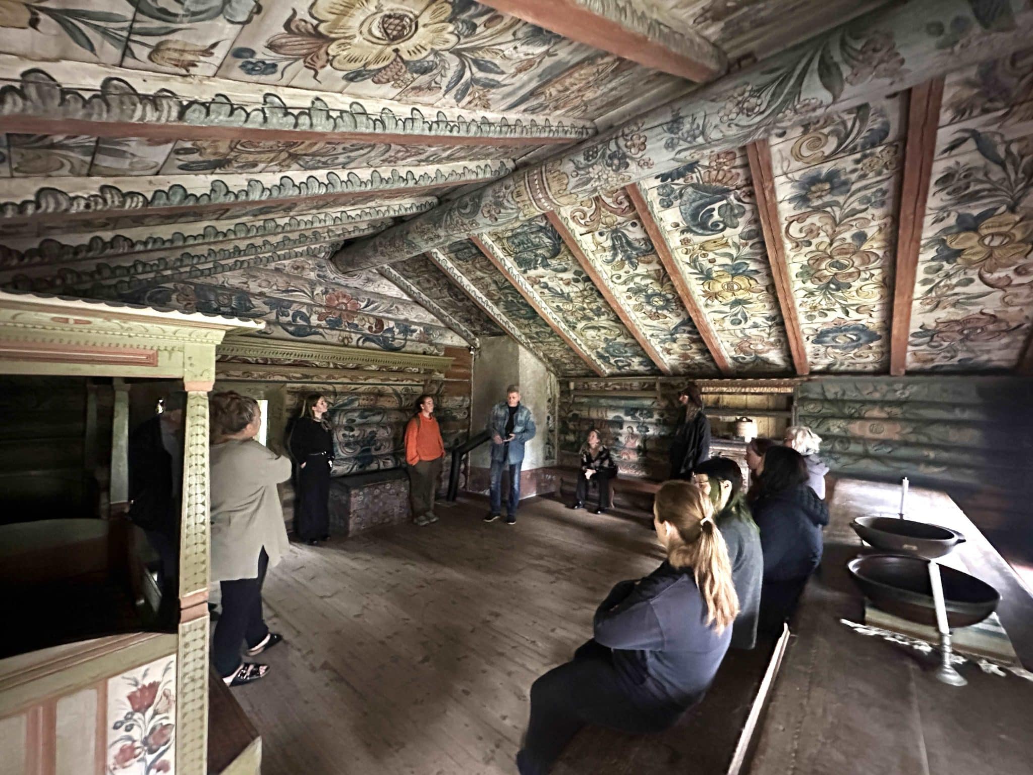 Rambergstua fra Heddal - nå i Brekkeparken. Bilder viser interiør og rosemaling i tak og på vegger i oppstua, gjestestua i andre etasje. En gruppe mennesker sitter og hører på en mann som forteller om Ola Hanssons rosemaling.