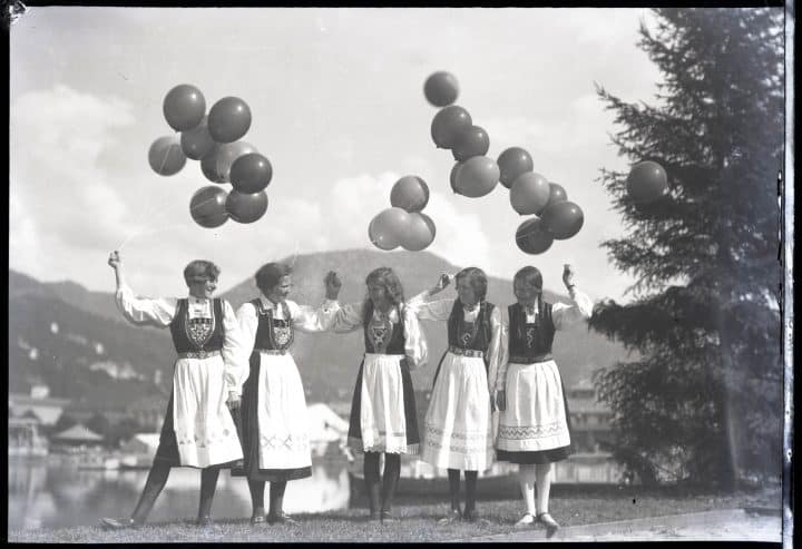 Fem unge kvinner i folkedrakt holder på ballonger og ler. Fotograf: Jensen Atelier, sort-hvitt bilde