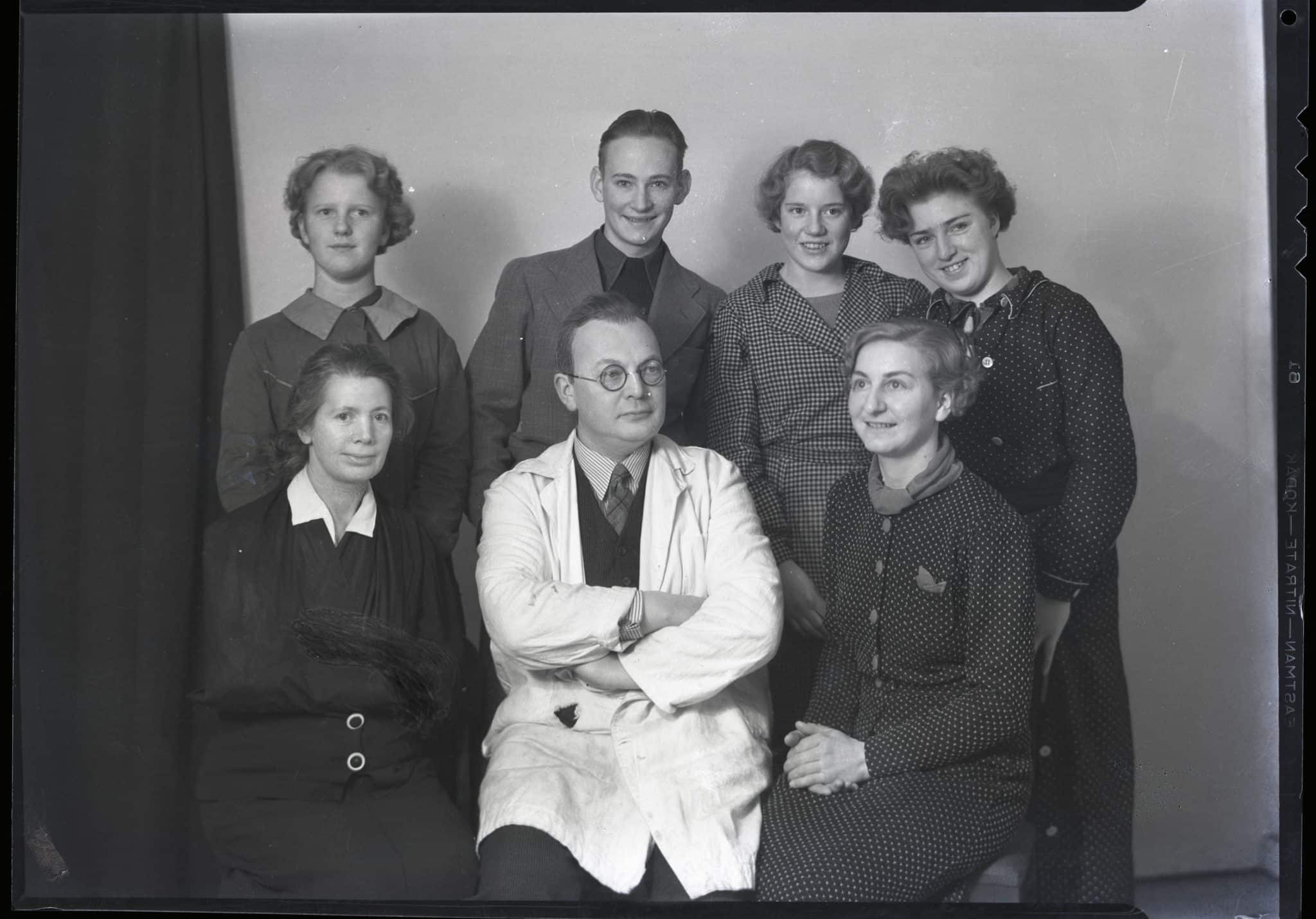 Sort-hvittfoto av Einar Jensen, som sitter i midten av gruppen. Bakerste rad fra venstre: Ukjent Alfhild Andreassen, ukjent gutt, Henny Dolva (1922 -2012) og Edith Johannesen (Borgestad).