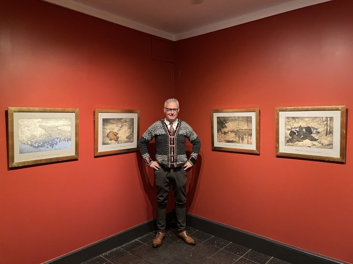 Sverre Følstad, konservator, kurator og kunsthistoriker ved Blaafarveværket foredrar om Tirelill Tove-serien. Følstad poserer foran en rød vegg, der fire bilder fra serien vises.