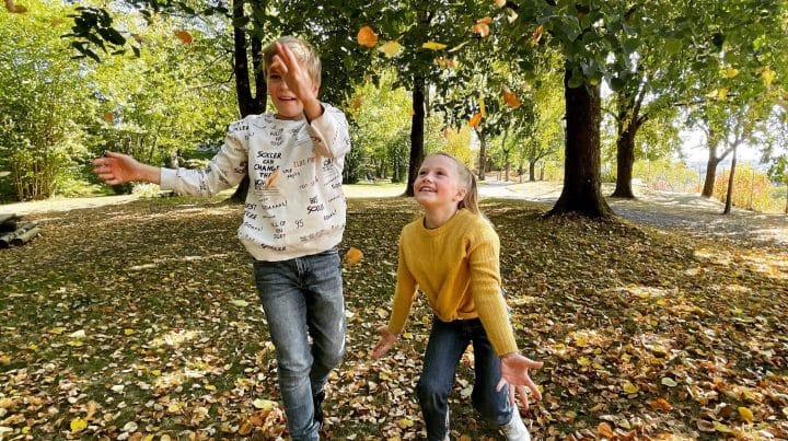 Høstferie, bilde av to barn som leker med høstblader i parken